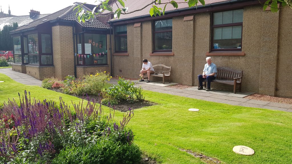 Church garden from Kildary Road with two people sat on the benches