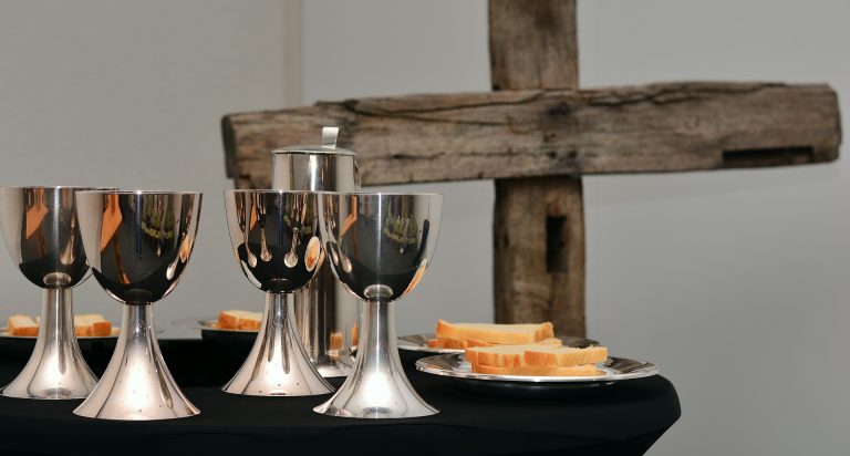 image of goblets and bread for communion with part of wooden cross in background